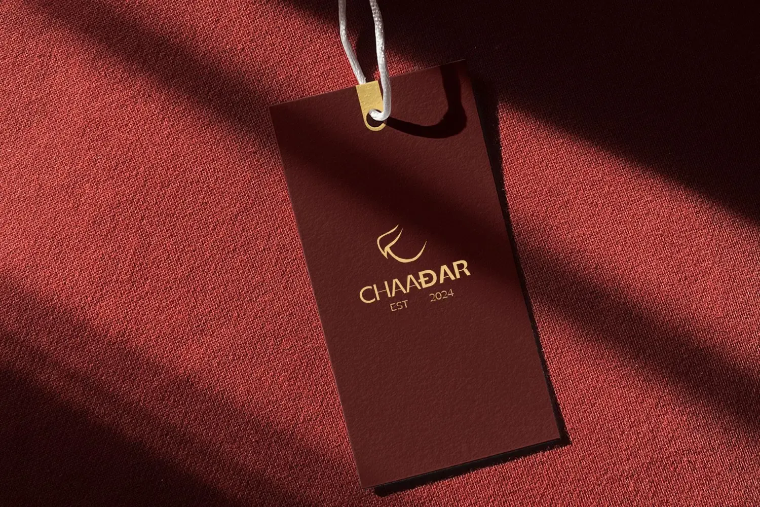 Chaadar: the gold Chaadar logo on a maroon swing tag resting on red wool